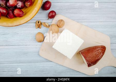 vista dall'alto di formaggio affumicato e feta su un tagliere in legno con noci e uva dolce su sfondo rustico Foto Stock