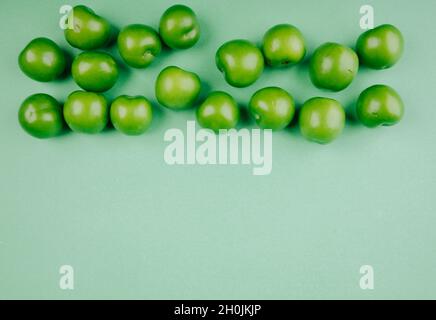 vista dall'alto delle prugne aculente verdi isolate su sfondo verde con spazio di copia Foto Stock
