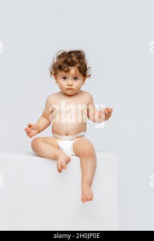 Ritratto verticale del bambino piccolo carino, bambino in seduta del pannolino, labbra di pointing isolate su sfondo bianco studio. Dolce infanzia Foto Stock