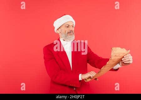 uomo maturo in santa hat lettura lettera su carta artigianale isolato su rosso Foto Stock