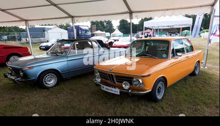 Vista frontale di tre quarti di una BMW Orange 2002 TII (E10) e di una Blue 2002 Cabriolet, in mostra al London Classic Car Show 2021 Foto Stock