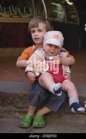ragazzino seduto su un gradino con un bambino in grembo Foto Stock