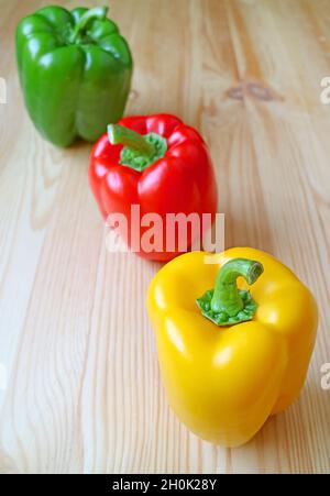 Peperoni tricolore allineati su sfondo di legno marrone chiaro Foto Stock