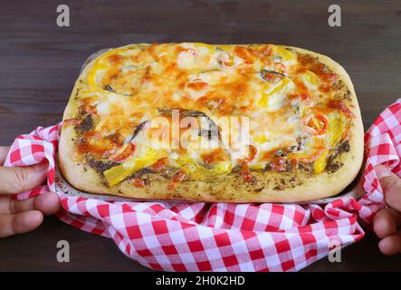 Mano dell'uomo che mette la pizza squisita del pesto veggie fatta in casa appena sfornata sul tavolo Foto Stock