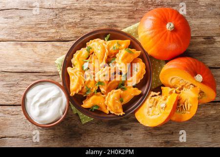 Deliziosi gnocchi di zucca d'arancia sani serviti con crema acida in primo piano in un piatto sul tavolo. Vista dall'alto orizzontale Foto Stock