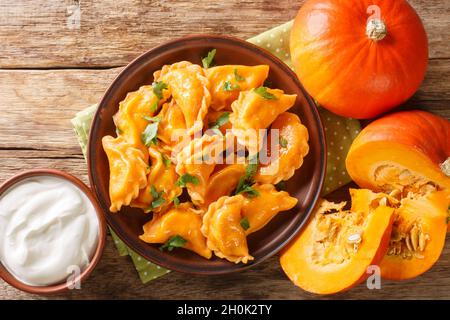 Gnocchi di zucca vegetariani cotti serviti con panna acida in primo piano su un piatto sul tavolo. Vista dall'alto orizzontale Foto Stock