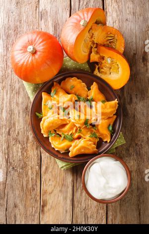 Gnocchi di zucca ucraini fatti in casa serviti con crema acida primo piano in un piatto sul tavolo. Vista dall'alto verticale Foto Stock