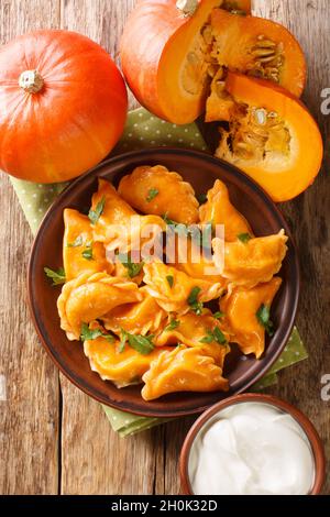 Gnocchi di zucca Pierogi autunnali serviti con panna acida in primo piano in un piatto sul tavolo. Vista dall'alto verticale Foto Stock