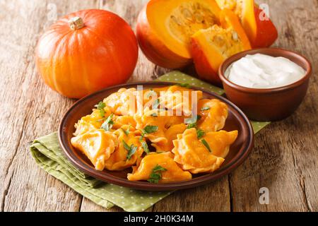 Gnocchi di zucca di stagione fatti in casa con erbe servite con panna acida primo piano su un piatto sul tavolo. Orizzontale Foto Stock