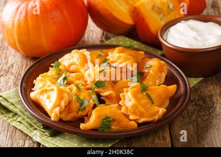 Deliziosi gnocchi di zucca d'arancia sani serviti con panna acida in primo piano in un piatto sul tavolo. Orizzontale Foto Stock