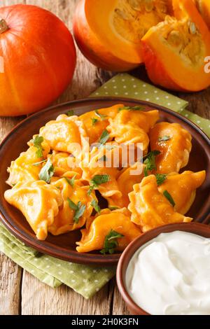 Autunno Pierogi gnocchi di zucca serviti con panna acida primo piano in un piatto sul tavolo. Verticale Foto Stock