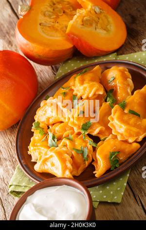 Gnocchi di zucca ucraini fatti in casa serviti con panna acida primo piano in un piatto sul tavolo. Verticale Foto Stock