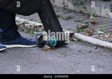 Un uomo che utilizza un soffiatore a foglia per raccogliere la caduta del congedo autunnale su un azionamento del tarmac Foto Stock