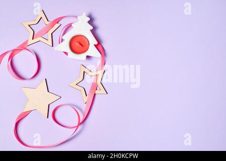 Flatlay di Natale con albero di natale, candela, stelle e nastro rosa su sfondo viola con spazio copia Foto Stock