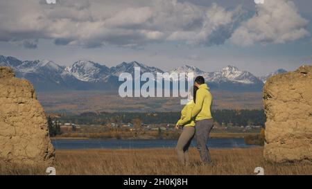 Uomo e donna in abbigliamento sportivo giallo verde. Una coppia incantevole di viaggiatori si abbraccia e bacia vicino alla pietra vecchia godendo il paesaggio delle Highland. Foto Stock