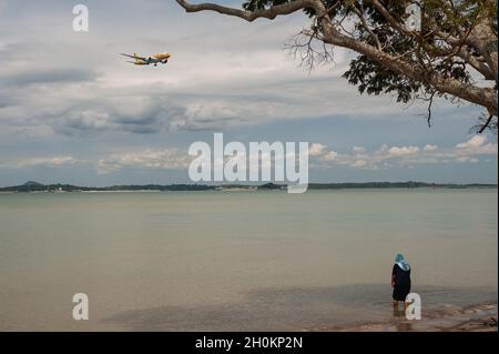 09.10.2021, Singapore, Repubblica di Singapore, Asia - Woman Wades attraverso l'acqua lungo la riva al Changi Beach Park mentre un aereo della Scoot Airlines si avvicina. Foto Stock