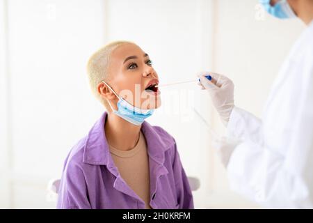 Signora millennial che fa il test pcr, ottenendo il test orale del tampone del coronavirus, medico femminile in costume medico protettivo Foto Stock