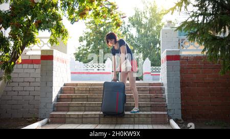 donna con una valigia pesante difficilmente sale le scale della stazione ferroviaria. Foto Stock