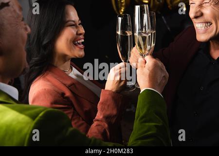 Amici interrazziali positivi che tostano champagne durante la festa di nuovo anno su sfondo nero Foto Stock