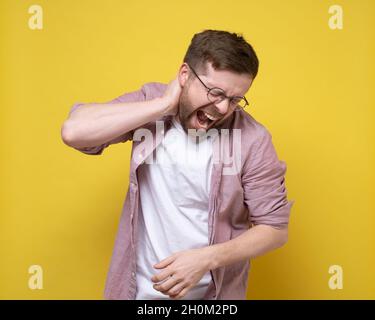 L'uomo sta avvertendo dolore severo nella zona del collo, tiene la mano alla zona infiammata ed urla con gli occhi chiusi. Foto Stock