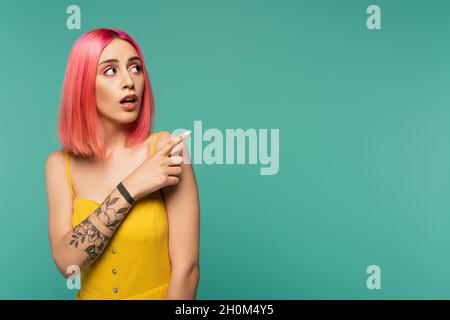 stupita giovane donna con capelli rosa tinti che poising con dito isolato sul turchese Foto Stock