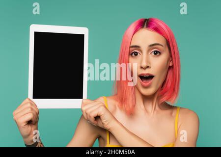 stupito giovane donna con capelli rosa tinti che reggono tablet digitale con schermo bianco isolato su blu Foto Stock