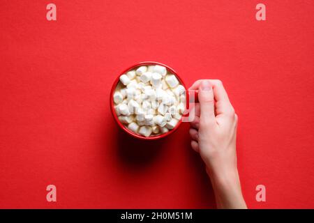 Tazza di cioccolata calda con marshmallows su sfondo rosso. Disposizione piatta, vista dall'alto, sovratesta. Bevanda calda invernale o autunnale, bevanda gustosa Foto Stock