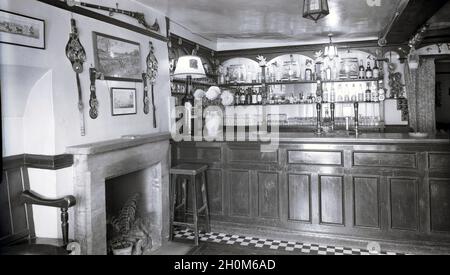 1950, storico, pub bar vuoto all'Angel Inn, Witney, Oxford, Inghilterra, Regno Unito che mostra un tradizionale banco bar con pompe a mano, ottica, sgabello e oggetti decorativi sopra il camino in marmo circonda. Foto Stock