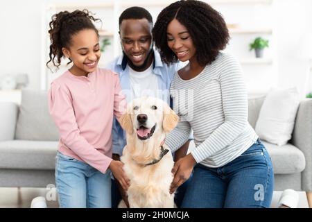 Giovane famiglia nera abbracciante con cane in posa a casa Foto Stock