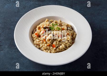 Risotto, riso italiano con funghi, verdure e prezzemolo servito su piatto di porcellana bianca Foto Stock