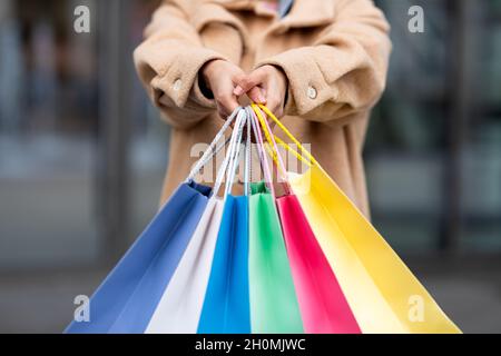 Vista croppata della giovane donna in caldo cappotto invernale che tiene colorati borse shopping all'aperto, primo piano Foto Stock