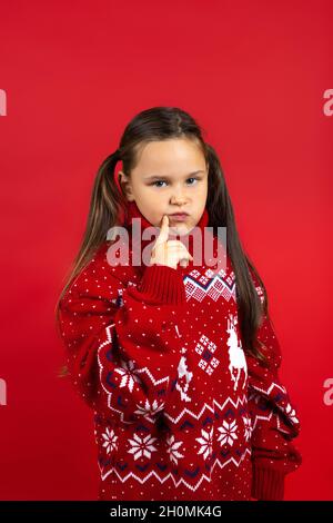 Primo piano ritratto di ragazza affascinante e sognante in maglia rossa Natale maglione con renna pensando al regalo, isolato su sfondo rosso Foto Stock