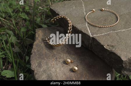 Moderni bracciali e orecchini a forma di spirale in oro a forma di catena su roccia all'aperto Foto Stock