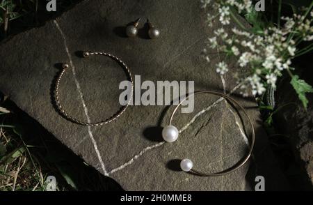 Vista dall'alto di braccialetti dorati e orecchini sulla roccia tra le piante Foto Stock