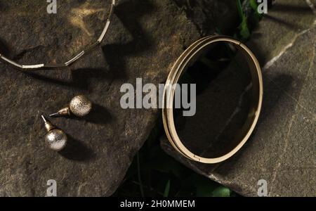 Moderno bracciale dorato lucido e orecchini su roccia all'aperto Foto Stock