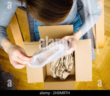 Vista dall'alto di una donna curiosa che sboxe in salotto nuova consegna di e-commerce ordinato merci via internee Foto Stock