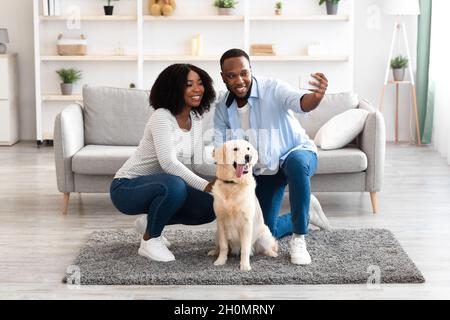 Giovane coppia nera che prende selfie con animale domestico in soggiorno Foto Stock