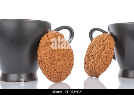 Due fragranti biscotti di farina d'avena di colore marrone scuro con due tazze, primo piano, isolati su bianco. Foto Stock