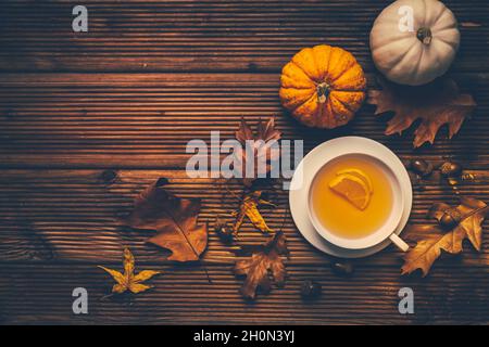 Tè caldo al limone con fogliame autunnale e zucche su sfondo di legno Foto Stock