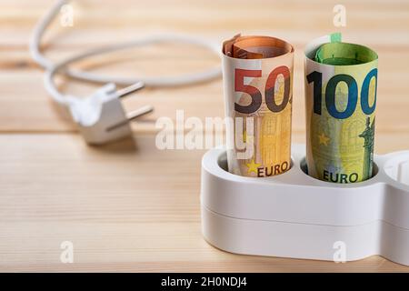 Banconote in euro inserite in una prolunga bianca su una superficie di legno. Energia costosa e aumento dei prezzi dell'elettricità. Foto Stock