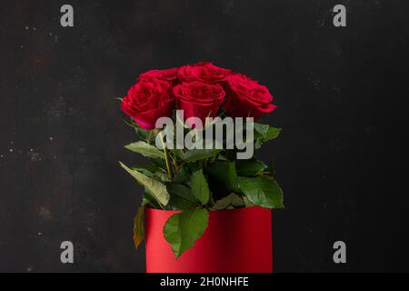 Bouquet di rose rosse in pentola rossa su sfondo scuro. Biglietto d'auguri per il giorno di San Valentino, il giorno delle donne. Concetto di vacanza. Foto Stock