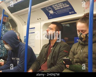 Londra, UK, 13 ottobre 2021: Molte persone sulla London Underground non indossano più maschere facciali, nonostante il trasporto per Londra abbia dei cartelli che ricordano ai passeggeri che una copertura facciale è una condizione di trasporto. Le persone possono viaggiare sui trasporti pubblici senza maschere facciali se hanno un'esenzione medica, ma la mancanza di applicazione significa che la masklessness è diffusa. Anna Watson/Alamy Live News Foto Stock