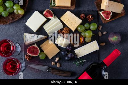 Varietà di formaggi, uva, fichi e noci su un piatto di ardesia. Spuntini di vino per una festa di vacanza. Vista dall'alto. Foto Stock