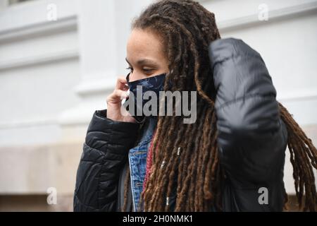 La donna mascherata parla sul telefono cellulare all'esterno mentre si trova in una pandemia globale Foto Stock
