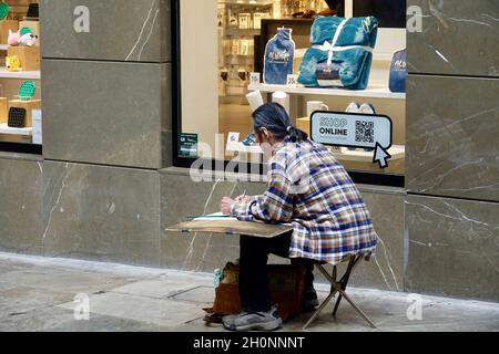 Granada, Spagna; ottobre-11, 2021: Uomo orientale che si disegna sulla strada accanto ad una vetrina Foto Stock