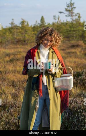 Ragazza gioiosa in trincea mano calda su tazza di tè caldo trascorrere il fine settimana godendo autunno soleggiato in campagna Foto Stock