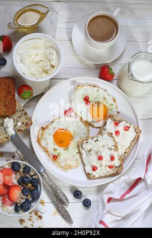 Colazione con uova fritte, muesli con frutta, frutti di bosco e caffè con latte su fondo di legno marrone Foto Stock