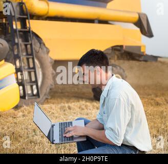 Giovane ingegnere con computer portatile davanti alla mietitrebbia sul campo Foto Stock
