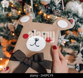 Immagine ravvicinata delle mani della donna che tengono i regali di natale avvolti davanti all'albero di natale. Foto Stock