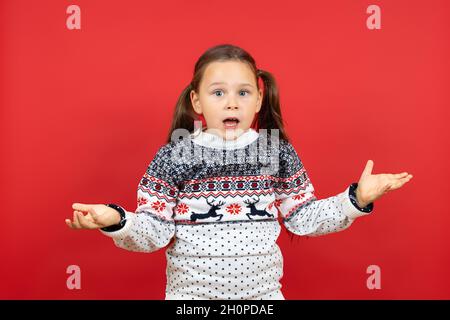 Ritratto di sorpresa, ragazza confuso in bianco maglione di Natale con le braccia renne spargimento, isolato su sfondo rosso Foto Stock